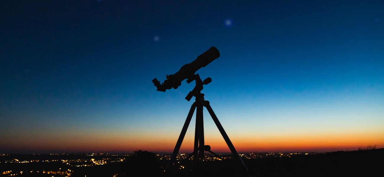 An astroglamping experience with a telescope silhouetted against the vibrant dusk sky.