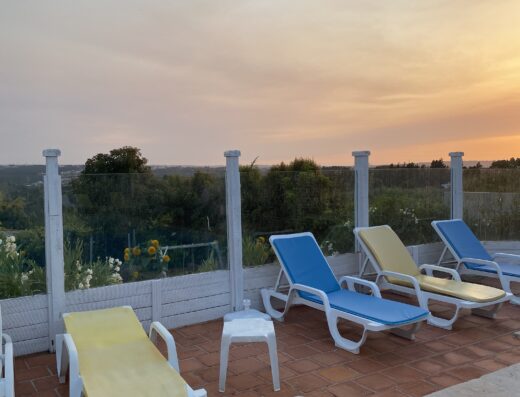 A group of lounge chairs on a rooftop overlooking a swimming pool at sunset.