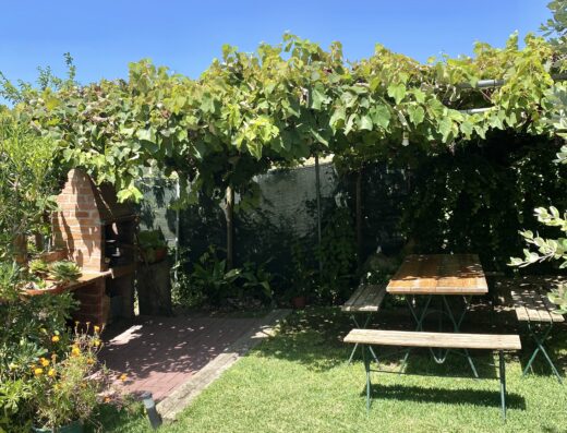A backyard with a table and chairs under a vine covered pergola.