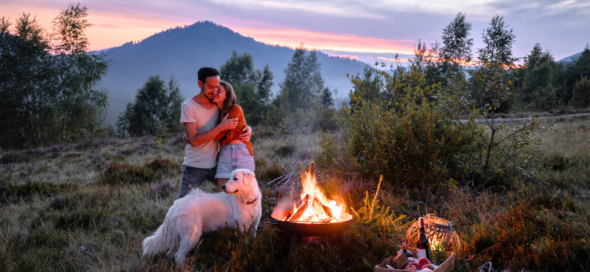 A couple with a dog enjoying the great outdoors as they gather around a campfire.