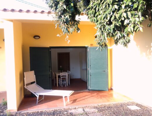A yellow house with green shutters and a lawn chair.
