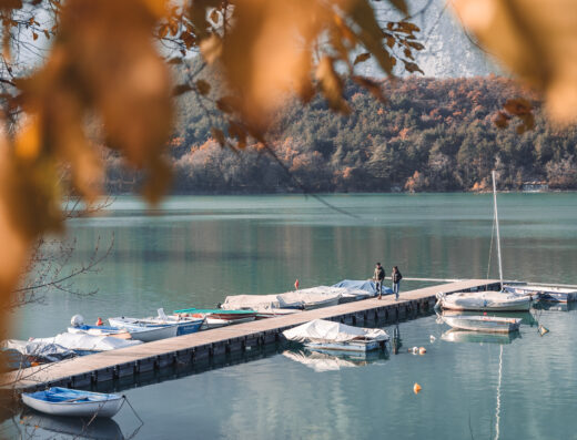A couple standing on a dock next to boats on a lake.