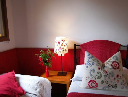 A cozy bedroom corner with a red and white theme, featuring a decorative lamp on a bedside table and a vase with red flowers.