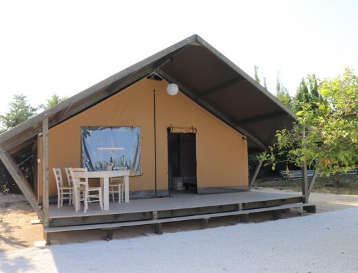 A canvas glamping tent with outdoor furniture on a wooden platform.
