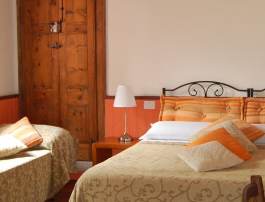 A cozy bedroom with twin beds, orange cushions, a bedside table with a lamp, and a wooden door in the background.