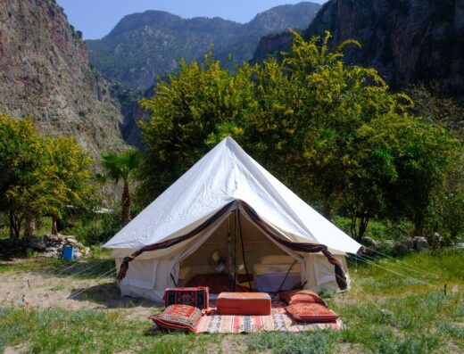 A white glamping tent set up in a scenic valley with mountains in the background.