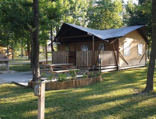 Glamping tent with wooden deck set in a tranquil wooded area.