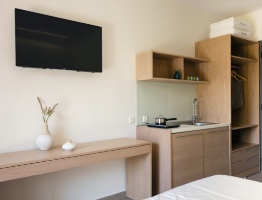 A modern, minimalist hotel room with a television, work desk, and kitchenette.