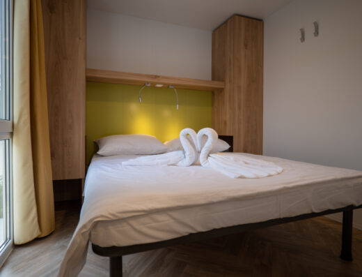 A neatly made bed with white linens and towels folded into swan shapes in a modern room with a yellow accent wall.