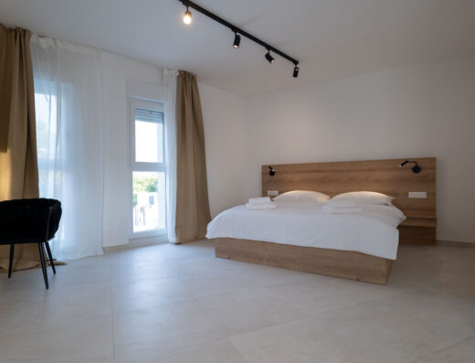 Minimalist and bright hotel room with a large bed, simple furnishings, and natural light.