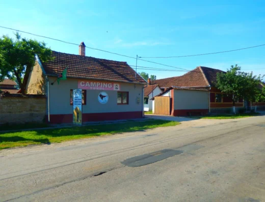A small camping facility building with signs, adjacent to a street in a quiet, sunny residential area.