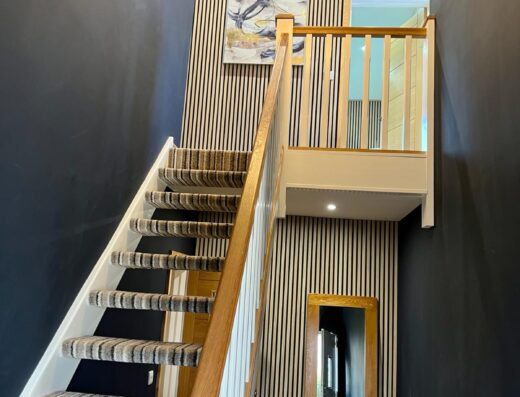Staircase with a striped carpet leading up to a second level in a modern home with dark walls and a wooden handrail.