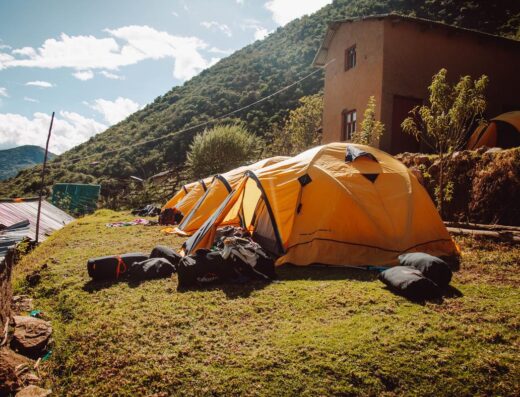 Orange tents set up in a grassy area near a house, with hills and trees in the background under a partly cloudy sky.