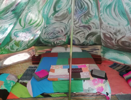 Interior of a colorful tent with a bed made up with patchwork quilts and blankets, some neatly folded.