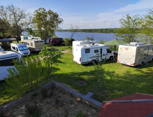 Campground by a lake with several parked RVs surrounded by trees and a clear blue sky.
