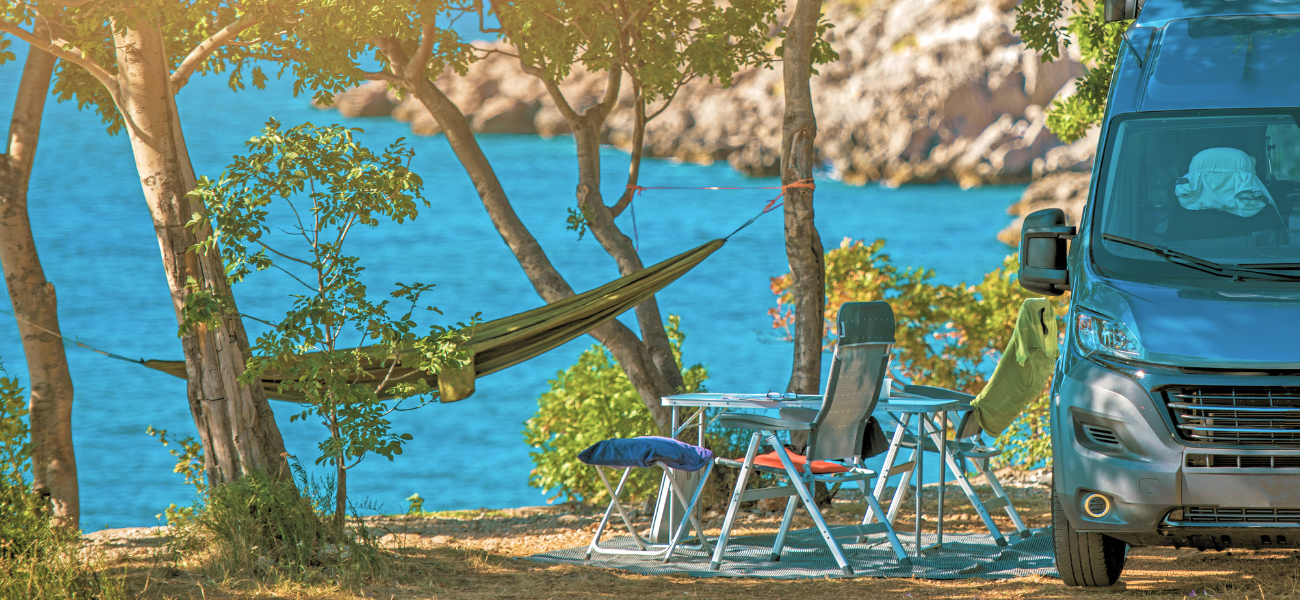 A camping vacation in Greece, with an RV parked next to the ocean and a hammock.